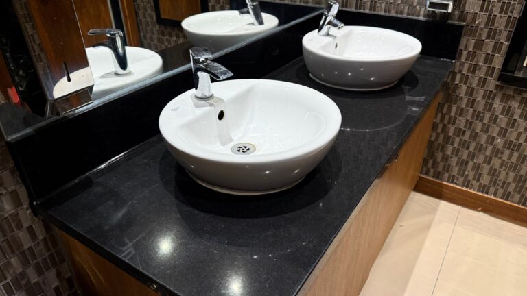 Black granite vanity with white bowl basins in a commercial washroom