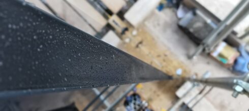Dark grey metal coping with rain droplets, scaffold below