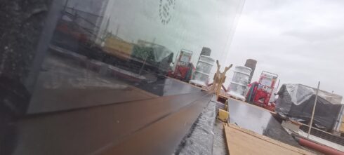 Glass screen set in a dark grey channel on a roof terrace under construction
