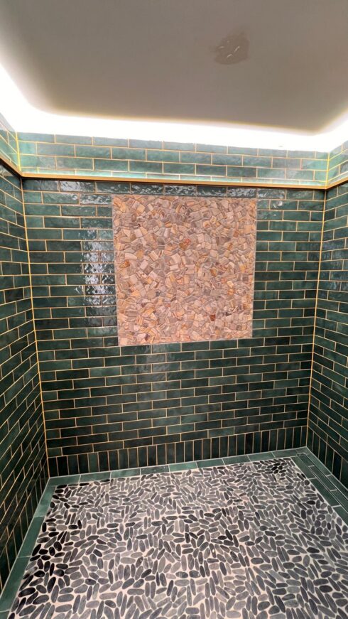 Green metro-tiled shower with mosaic feature panel and pebble floor, joints sealed