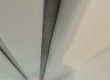 Long grey sealant joint along white wall panels, seen from below