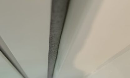 Long grey sealant joint along white wall panels, seen from below