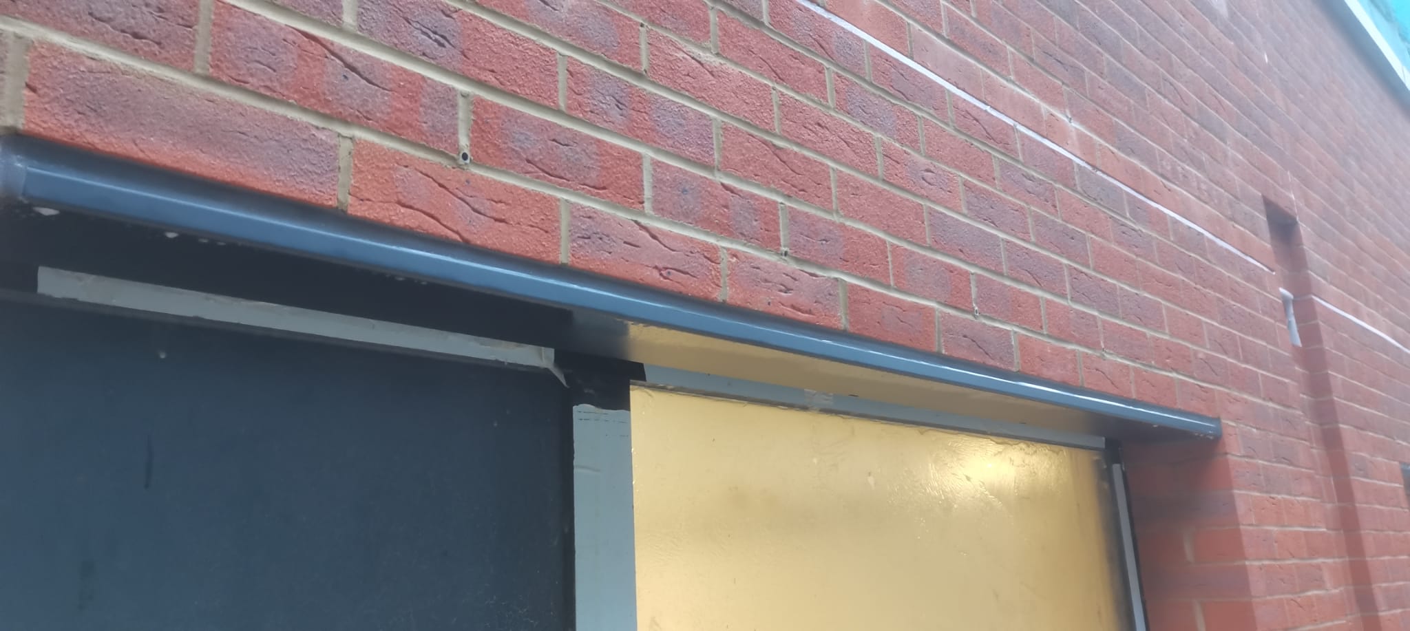 Grey window head flashing set into red brickwork with a sealed joint