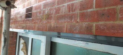 Grey aluminium window head below red brickwork, sealed at the joint