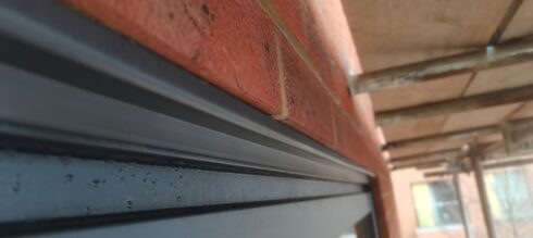 Grey aluminium window sill below red brickwork with a sealed joint