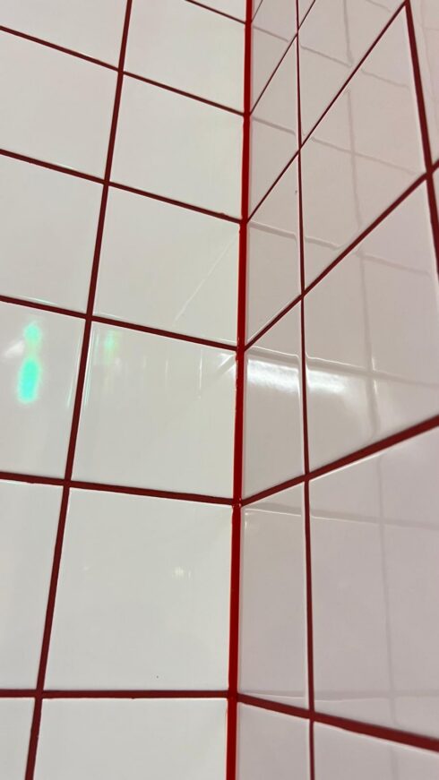 Internal corner of white wall tiles sealed with red sealant to match the red grout