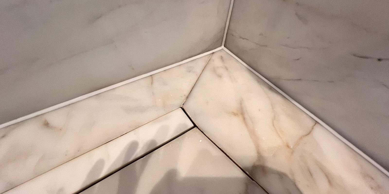 Fine white silicone joints where a marble shower floor meets the marble wall tiles