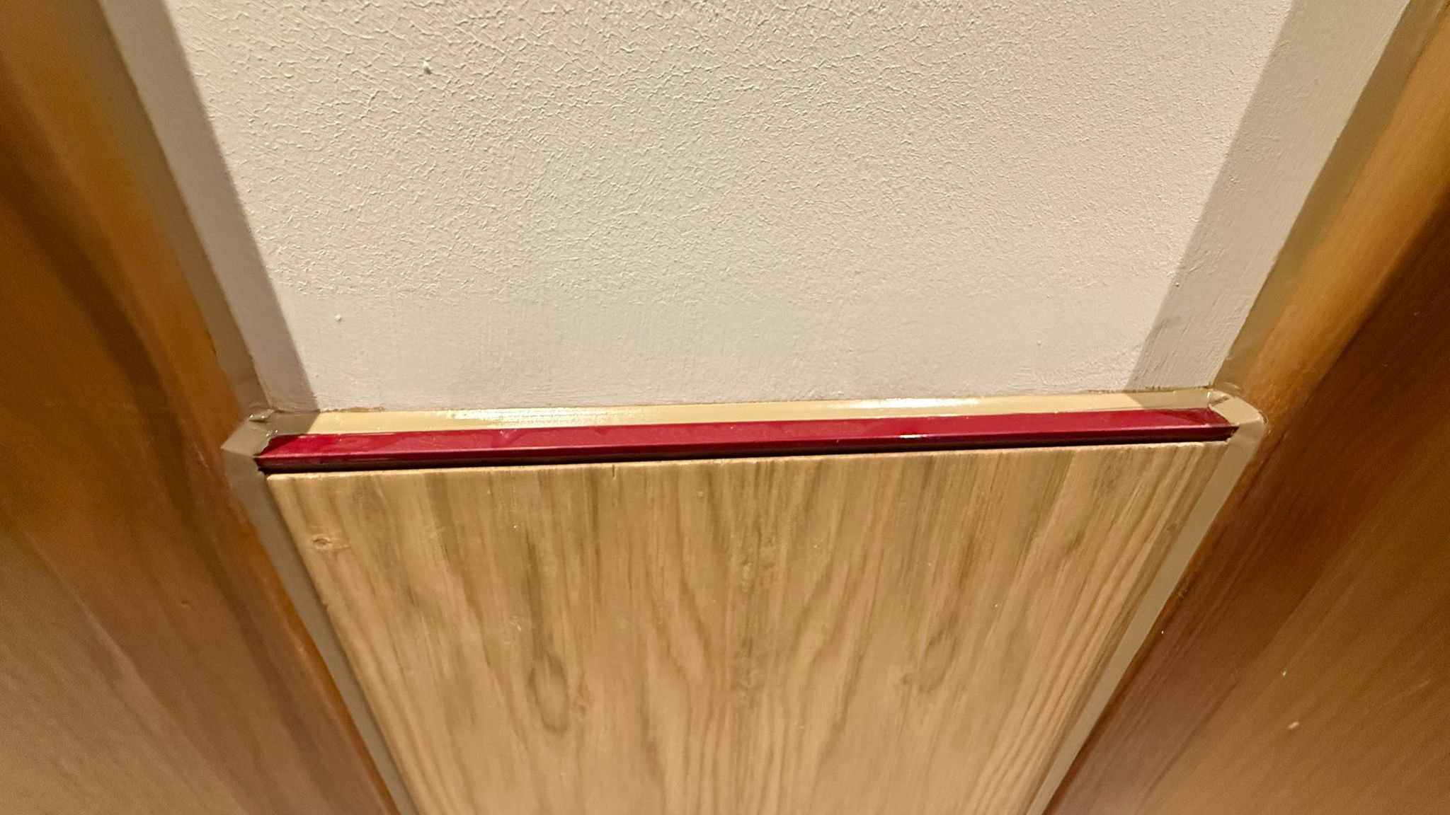 Red capping on oak panelling below a white wall, joint sealed