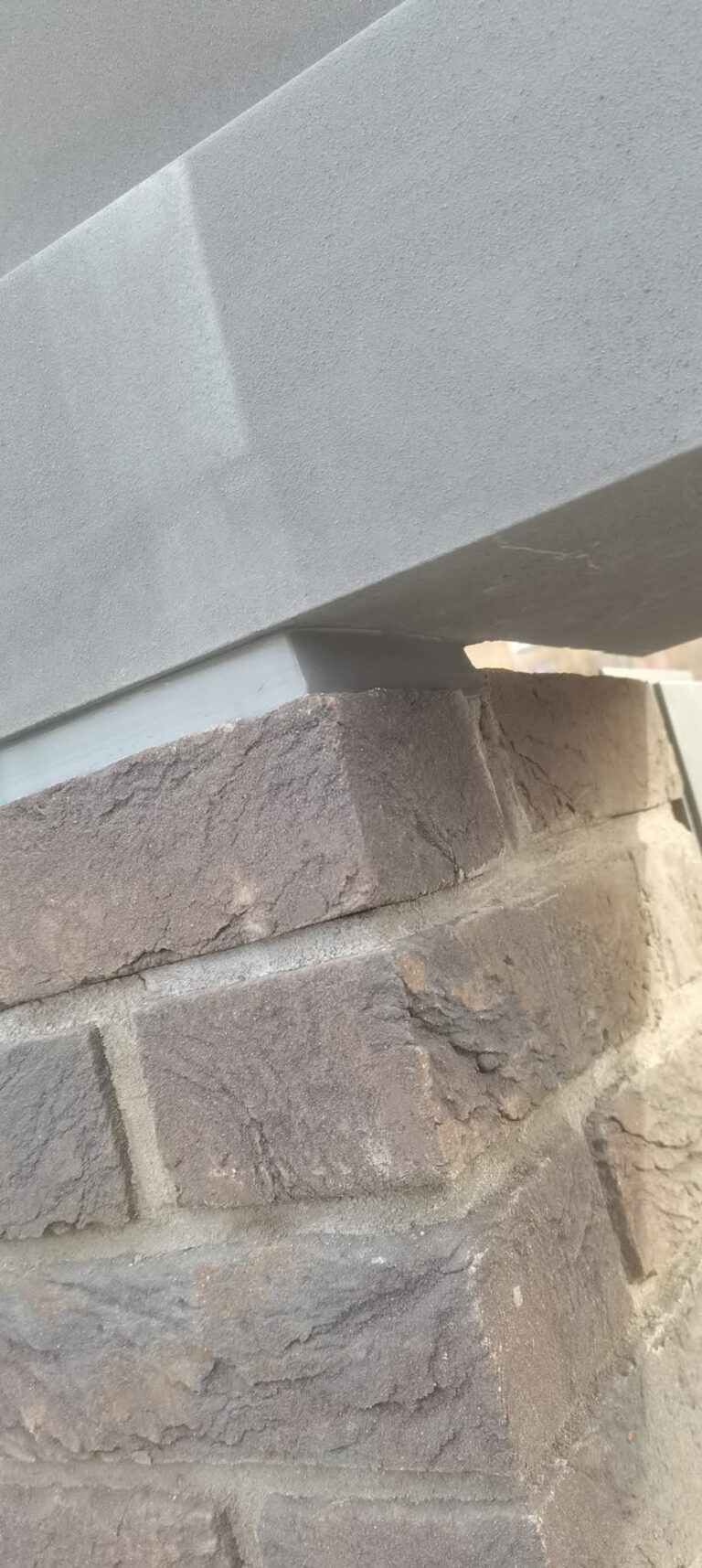 Grey stone coping on a dark brick pier with a sealed joint