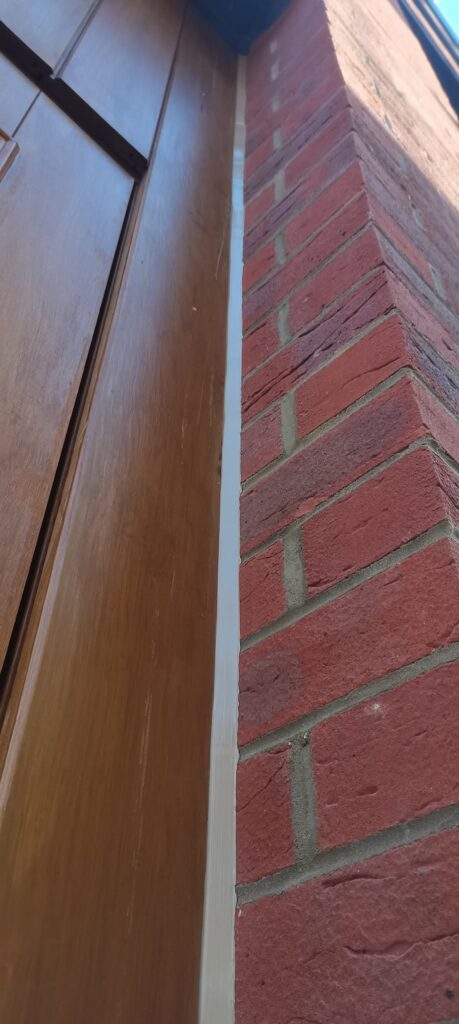 Light-coloured sealant joint between timber-effect cladding and red brick