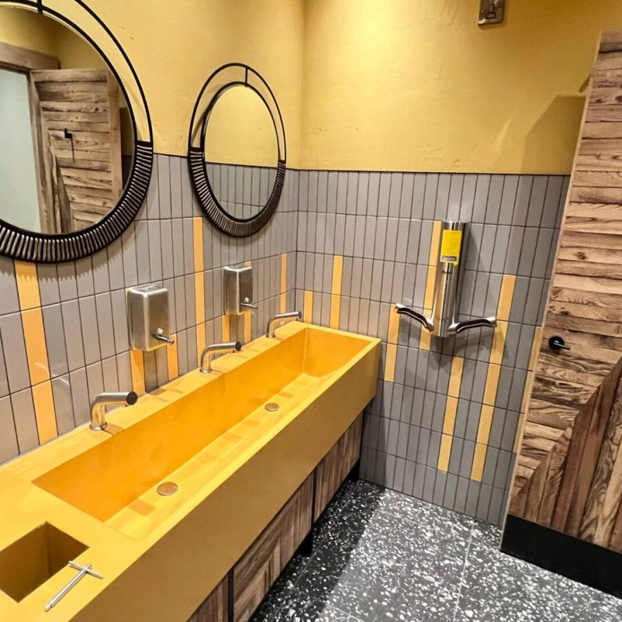 Washroom with yellow trough basin, round mirrors and terrazzo floor, sealed and finished