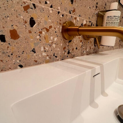 White basin with a brass wall-mounted tap against terrazzo tiling
