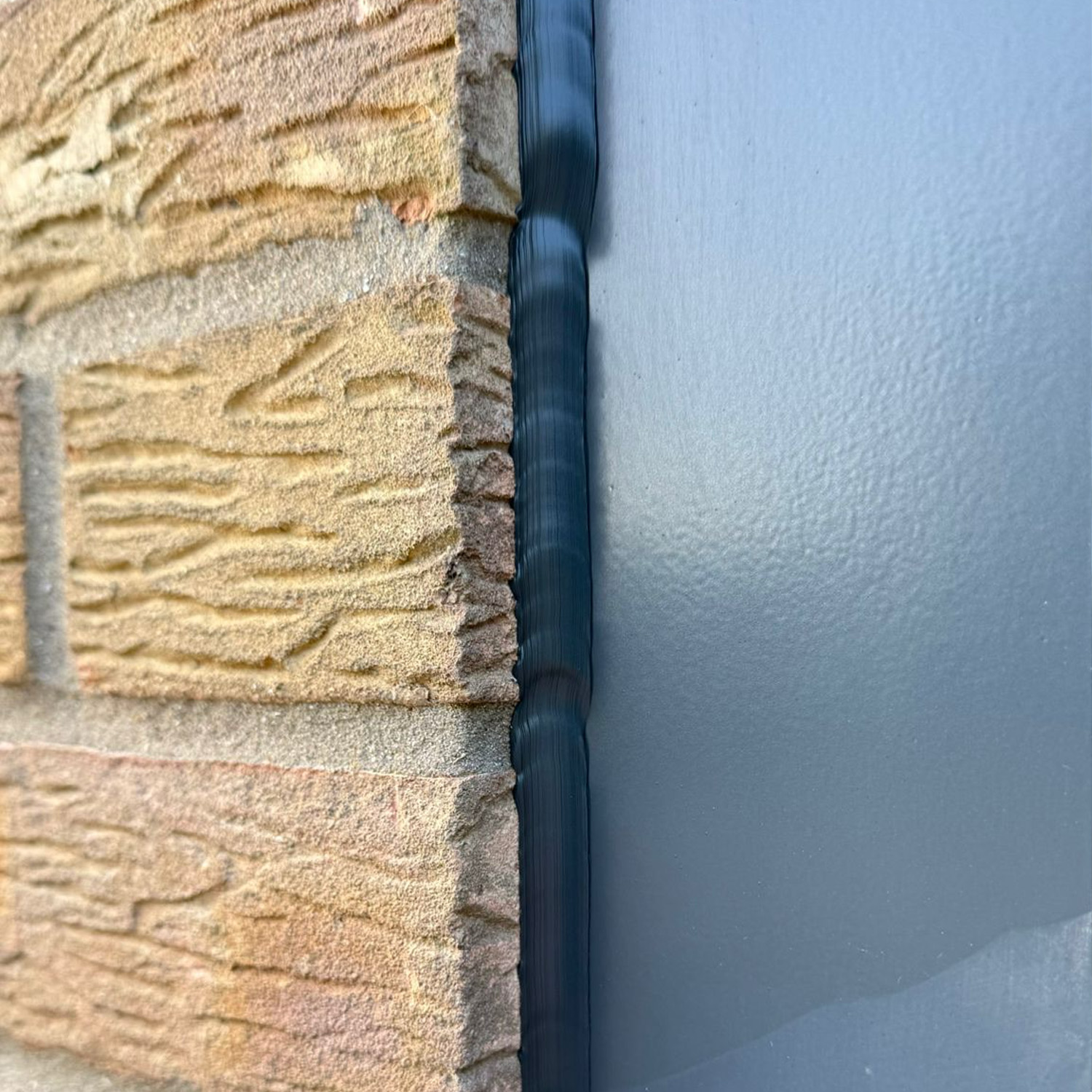 Before: lumpy, untidy old sealant between an anthracite window frame and buff brick