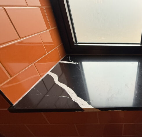 Black quartz window sill with dark sealant joints to orange gloss metro tiles and a black window frame