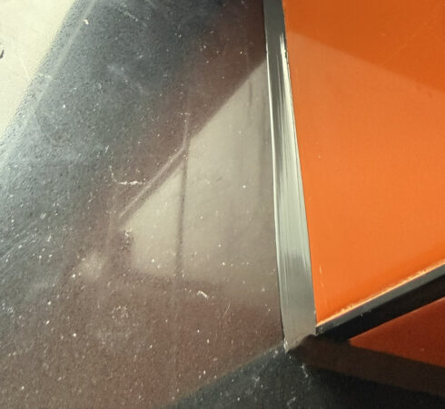 Fresh black sealant run along the edge of orange tiles where they meet a black quartz window sill