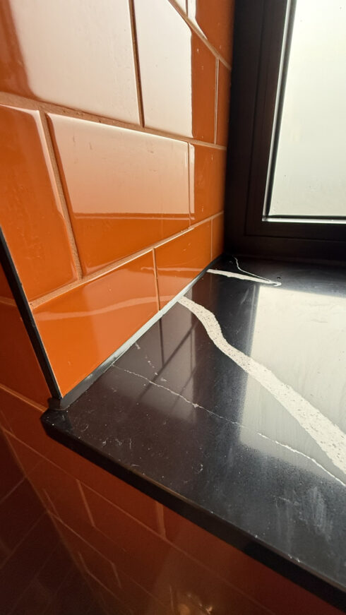 Neat black silicone joint along the line where orange gloss tiles meet a black quartz window sill