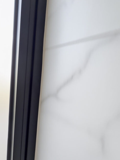 Black window frame sealed against white marble-effect wall tiles in a modern bathroom