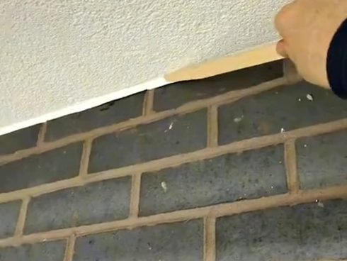 Tooling a sealant joint between white textured render and dark grey brickwork