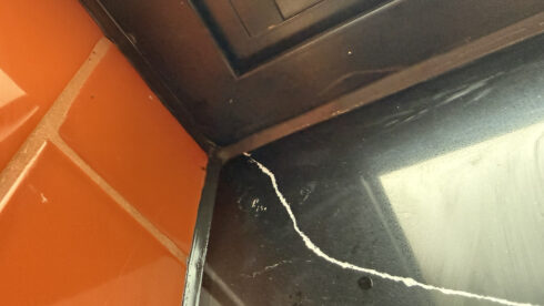 Close-up of a glossy black sealant joint where orange tiles, a black window frame and a quartz sill meet